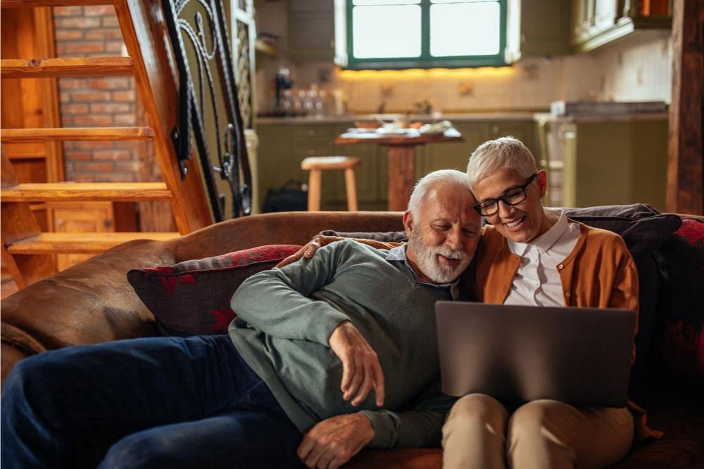 An elderly couple sitting on a couch, looking at a laptop together