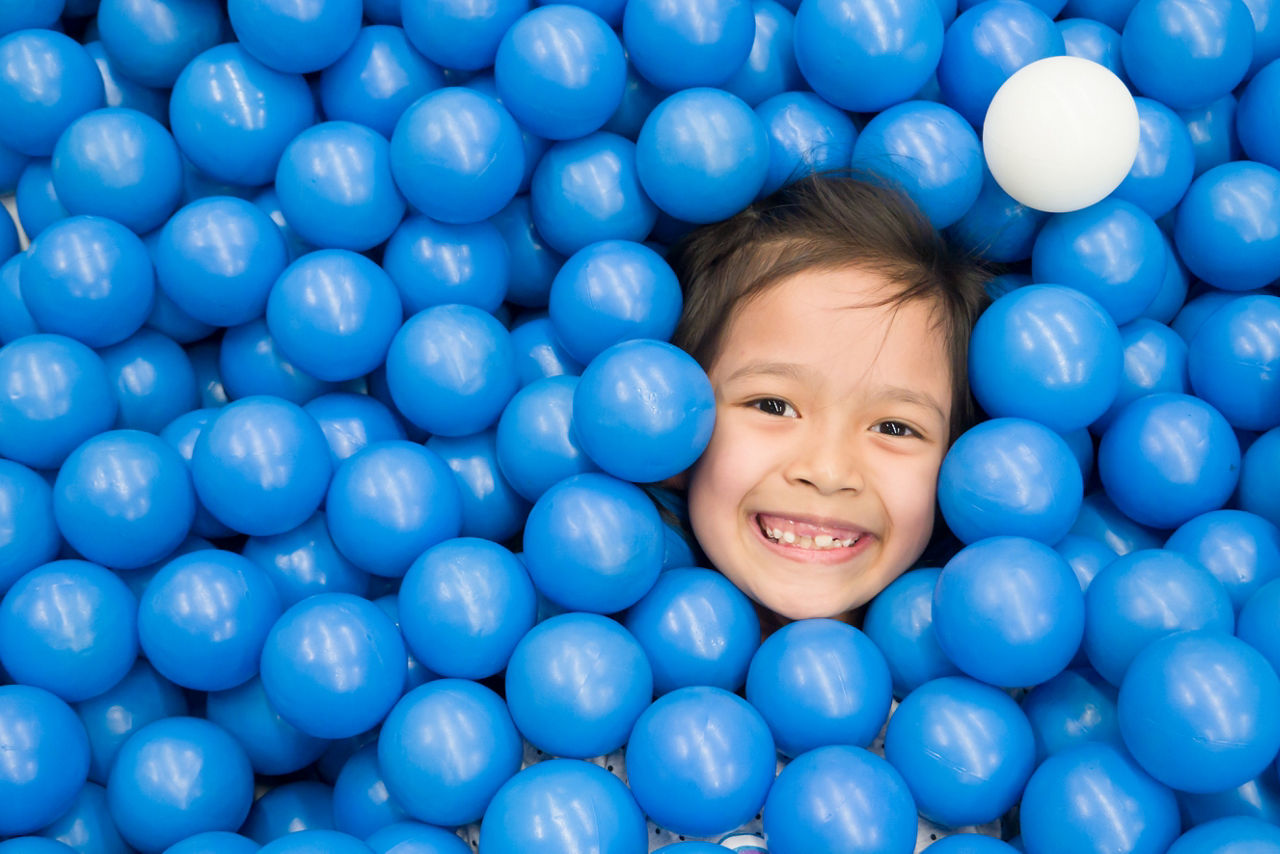 Asian kid in blue ball pond. Baby playing in dry ball pond indoor playground.