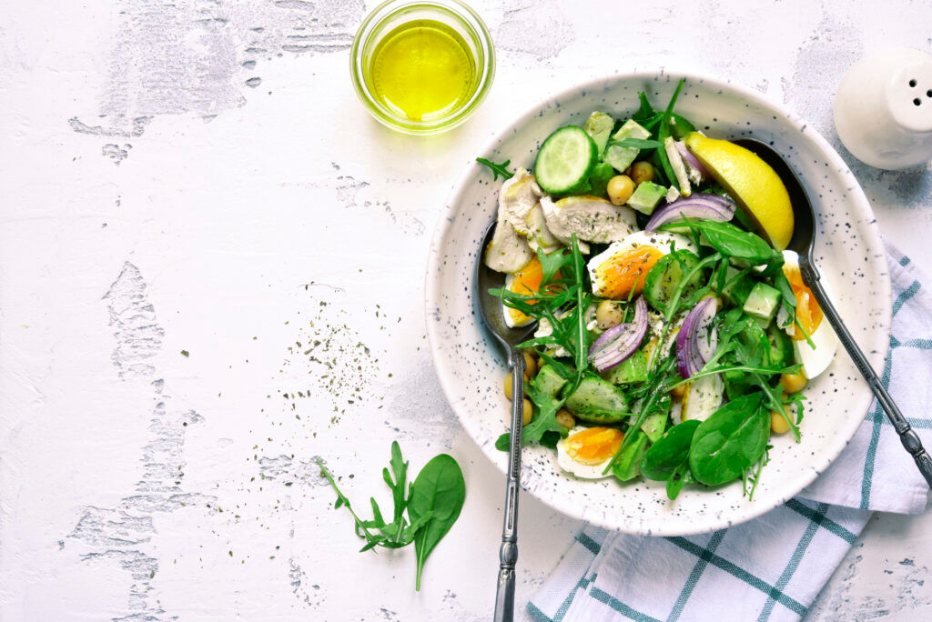 Green vegetable salad with chickpea,chicken fillet and boiled eggs on a white slate, stone or concrete background.Top view with copy space. (Green vegetable salad with chickpea,chicken fillet and boiled eggs on a white slate, stone or concrete backgro