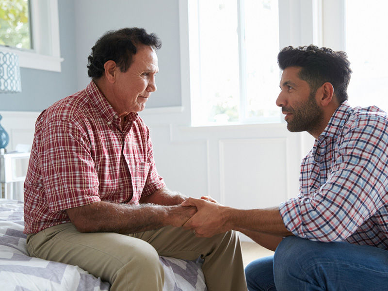 A man sitting on a bed, holding hands with someone