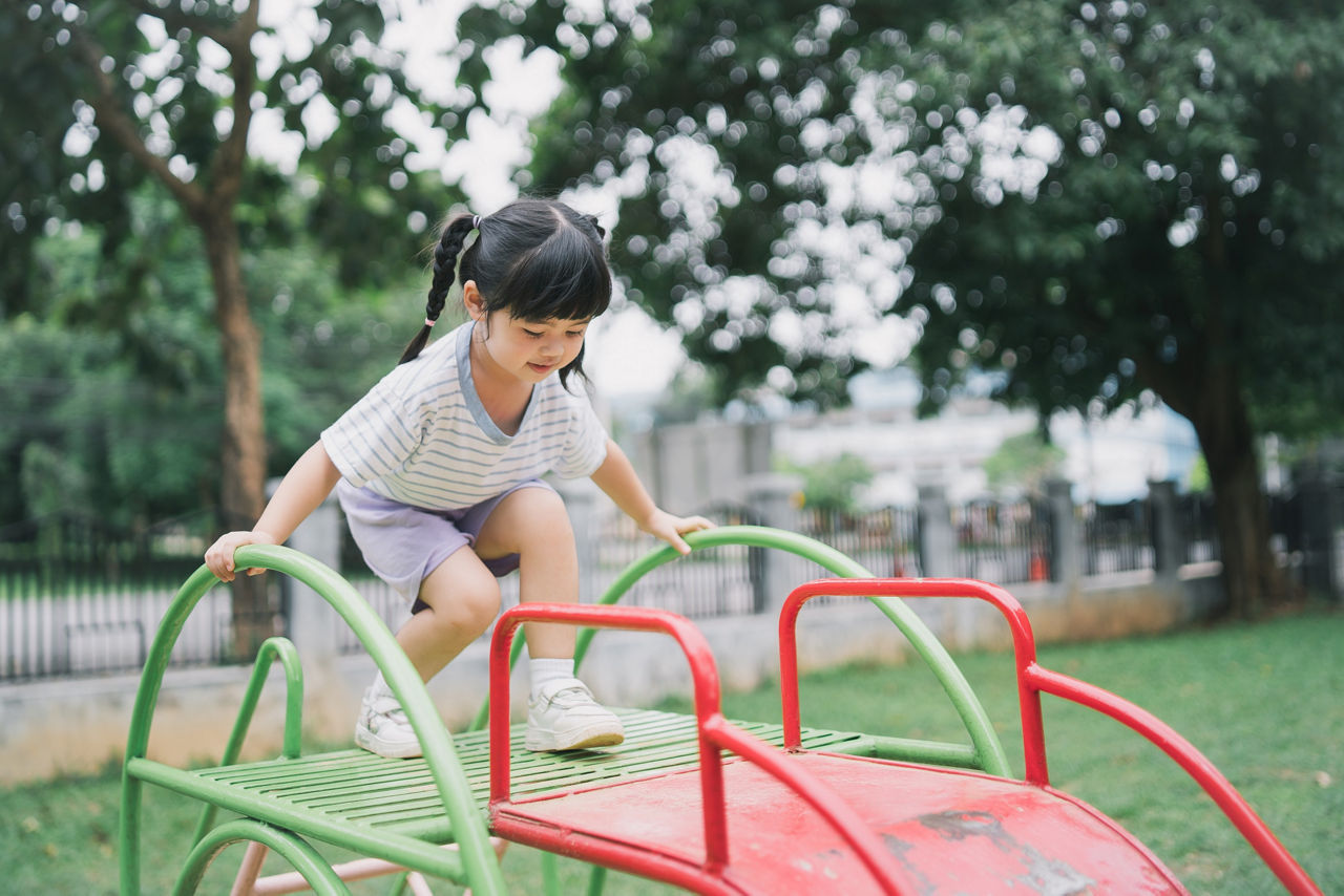 Cute asian girl play on school or kindergarten yard or playground. Healthy summer activity for children. Little asian girl climbing outdoors at playground. Child playing on outdoor playground.