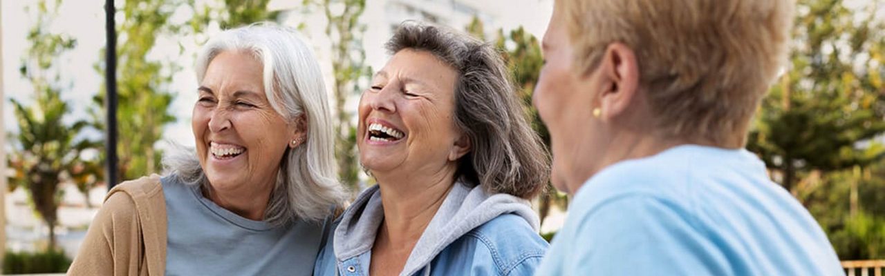 Oudere volwassenen lachen samen buiten in een groene omgeving tijdens een sociaal en actief moment.