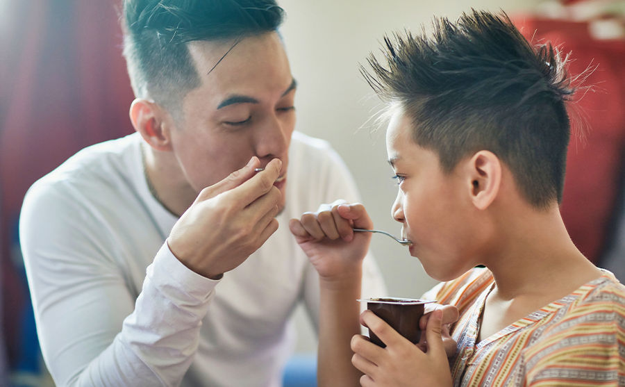 Image of a man and a child eating yogurt together.