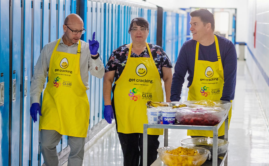 Image of two men and a woman walking together, the woman in the middle, pushing a cart of food.