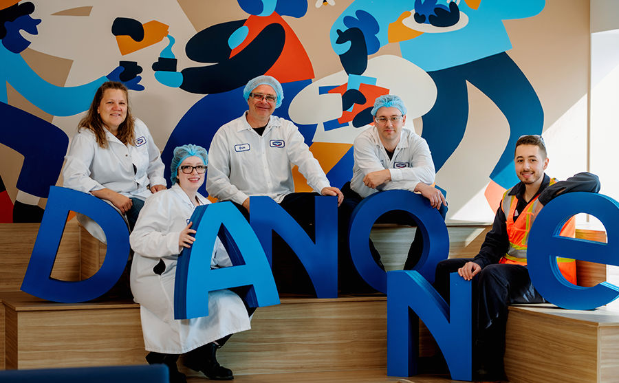 A diverse group of Danone Canada employees in uniform proudly pose with large "DANONE" letters.