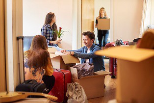 A group of four university students move into their shared flat , and start to unpack boxes. One male student is looking through his boxes in the foreground