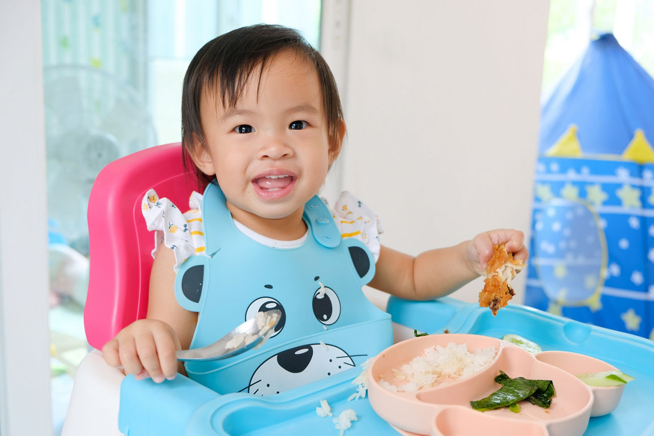 Asian toddler girl 1 year old Happy eating by herself with Baby Led Weaning (BLW) method, Self-Feeding