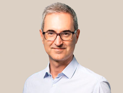 Frederic Guichard, President of Danone Canada, smiles confidently in a warm expression. He wears glasses, a light blue dress shirt, and has short gray hair.