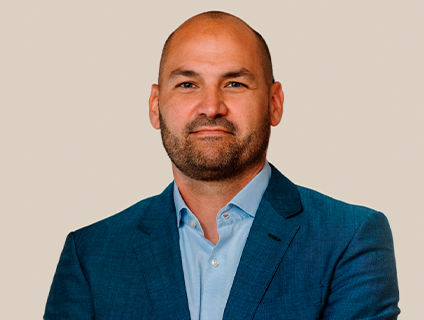 Iannick Melancon, Senior Vice President of Customer & Commercial Sales at Danone Canada, appears approachable with a beard and a genuine smile in his portrait. He wears a blue blazer over a light blue dress shirt and has a shaved head.