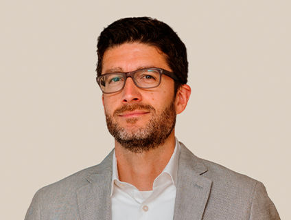 Marc Lavoie, Vice President of Finance at Danone Canada, sports a beard and glasses, offering a friendly smile in his portrait. He wears a light gray blazer over a white T-shirt and has short dark hair.