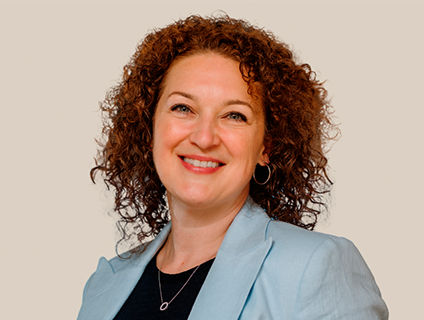 Mélanie Lebel, Senior Vice President of Human Resources at Danone Canada, smiling at her portrait. She wears a light blue blazer over a black T-shirt and has medium-length red curly hair.