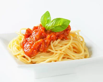 A close-up of freshly cooked spaghetti topped with vibrant tomato sauce and garnished with fresh basil leaves. The dish is presented on a clean white square plate, emphasizing its simplicity and elegance. The bright red sauce contrasts beautifully with the pale yellow pasta, creating a visually appealing meal.