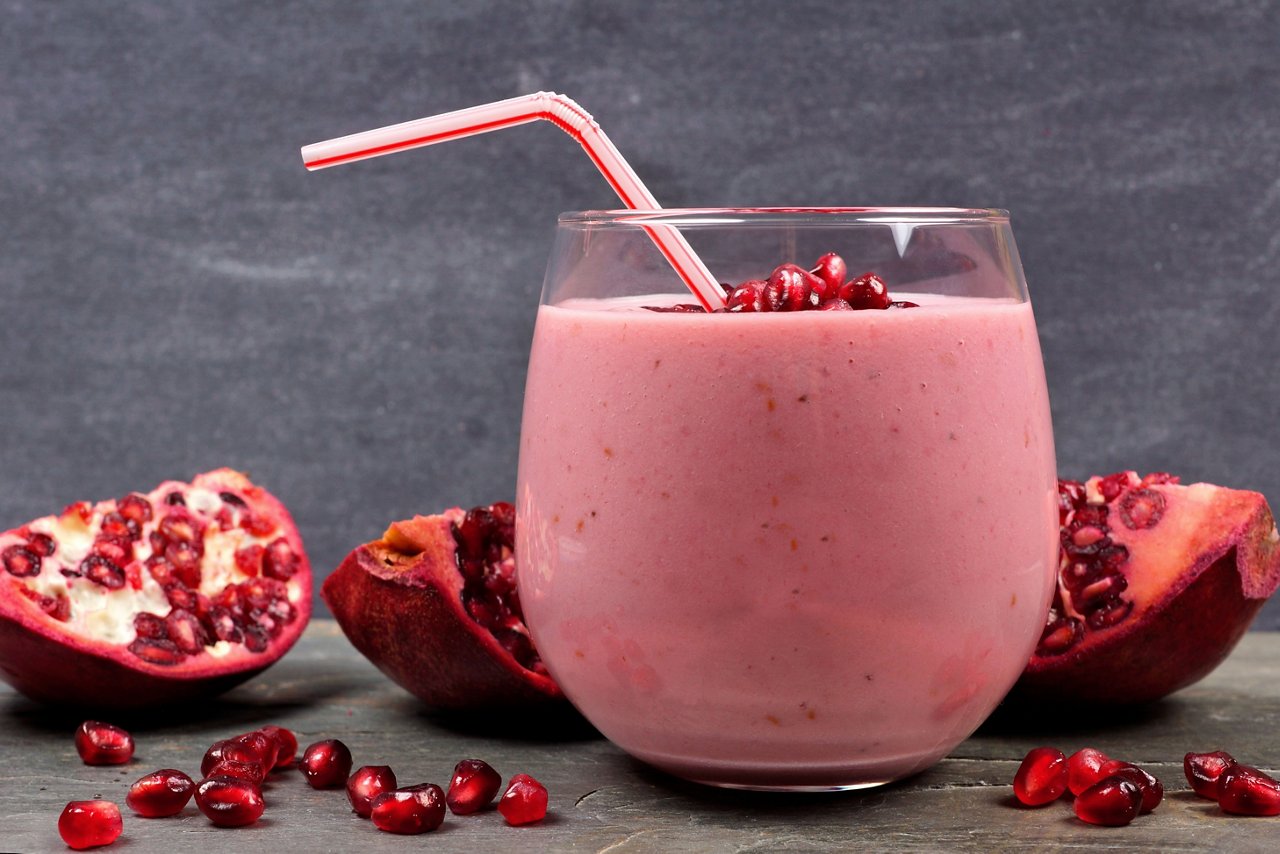 Pomegranate raspberry smoothie in a tumbler glass with pomegranate pieces, scene on black slate