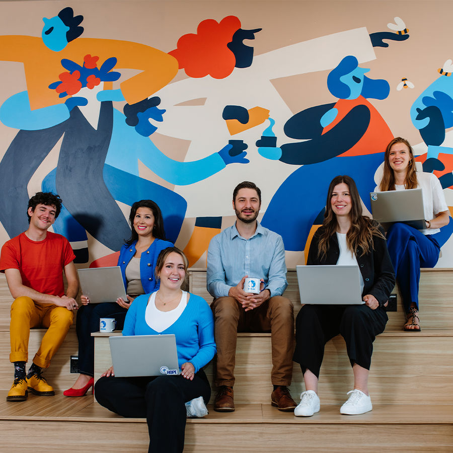 Image of six people who work at Danone, sitting on a wooden bench, looking forward and smiling. 