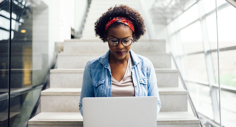 Focused young African female college student working on a laptop on some stairs on campus preparing for an exam