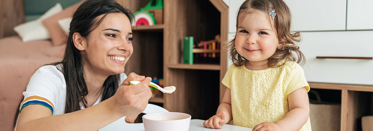 Young mother feeding her baby girl with a spoon at home