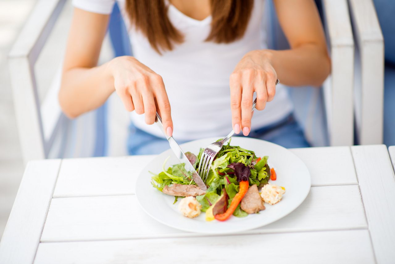 Break for energy, vitamins and refreshness. Close up cropped photo of lady, eating salad on a white modern wood table in an open air restaurant