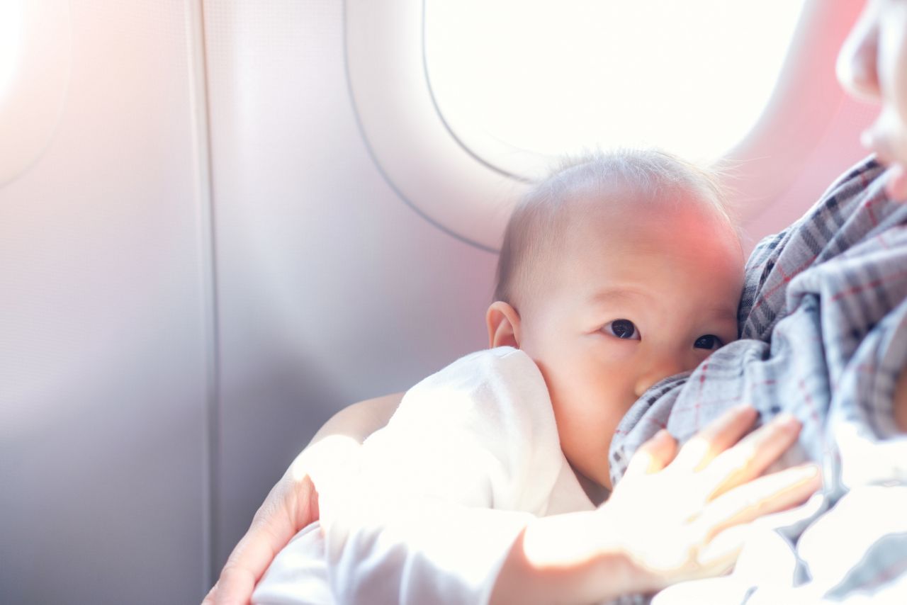 Asian mother is breastfeeding Cute little Asian 18 months toddler baby boy child on Airplane,Toddler lying on mother's laps, BreastFeeding in Public concept, harsh sunlight overexposed at baby hand