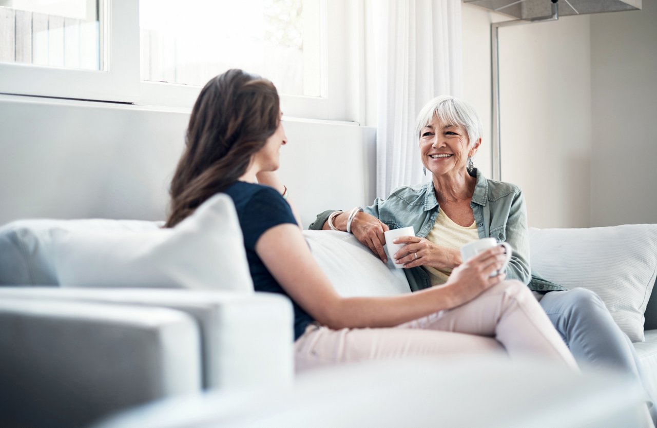 Junge Frau nimmt ältere Frau in den Arm bei einer Tasse Kaffee