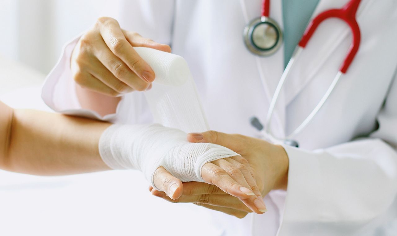 Close-up of female doctor with stethoscope bandaging hand of patient. (Selective Focus)