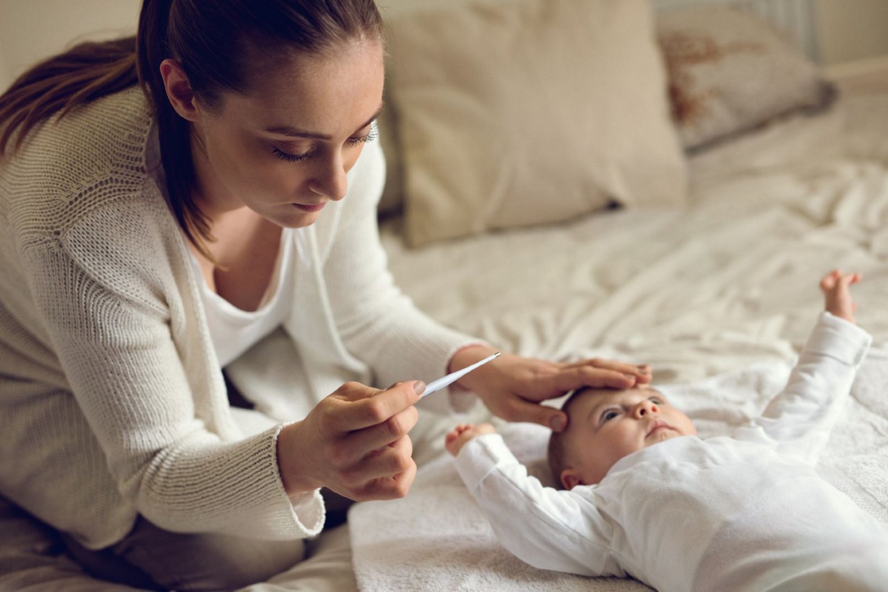 Mutter mit Fieberthermometer fühlt Babys Stirn