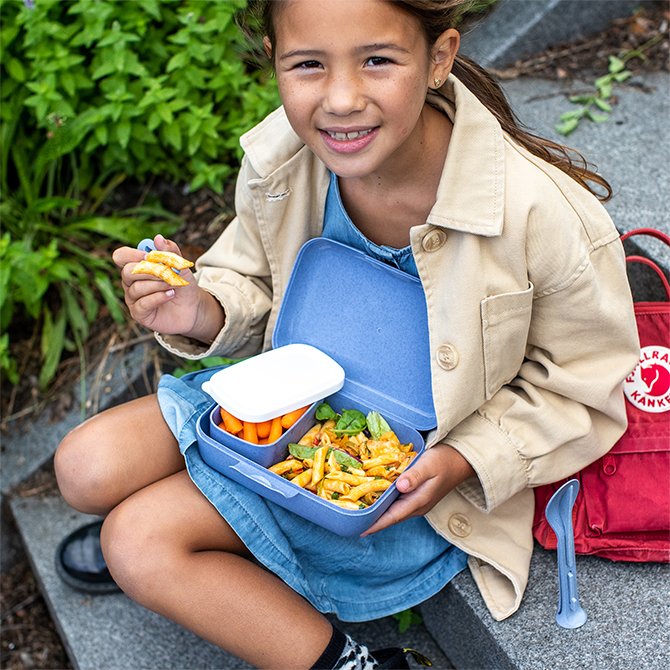 Kind hält stolz gefüllte Lunchbox auf dem Schoß
