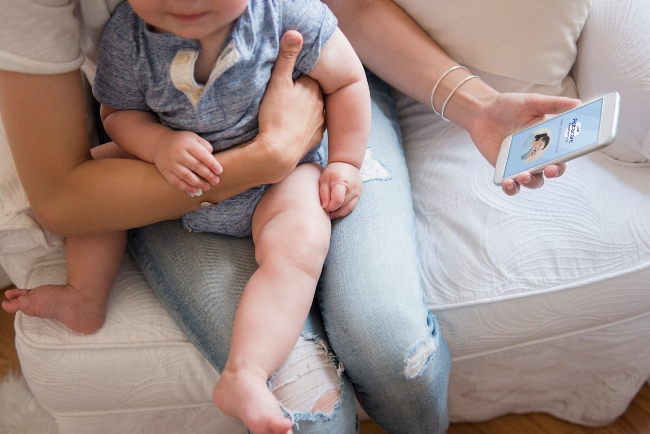 Baby sitzt bei Mutter auf dem Schoss und Mutter hat zusätzlich das Handy in der Hand