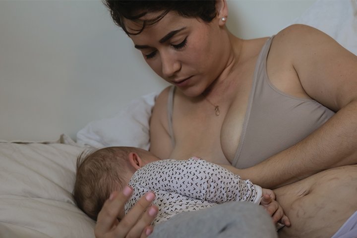 Mama liegt mit Baby im Bett und stillt Baby