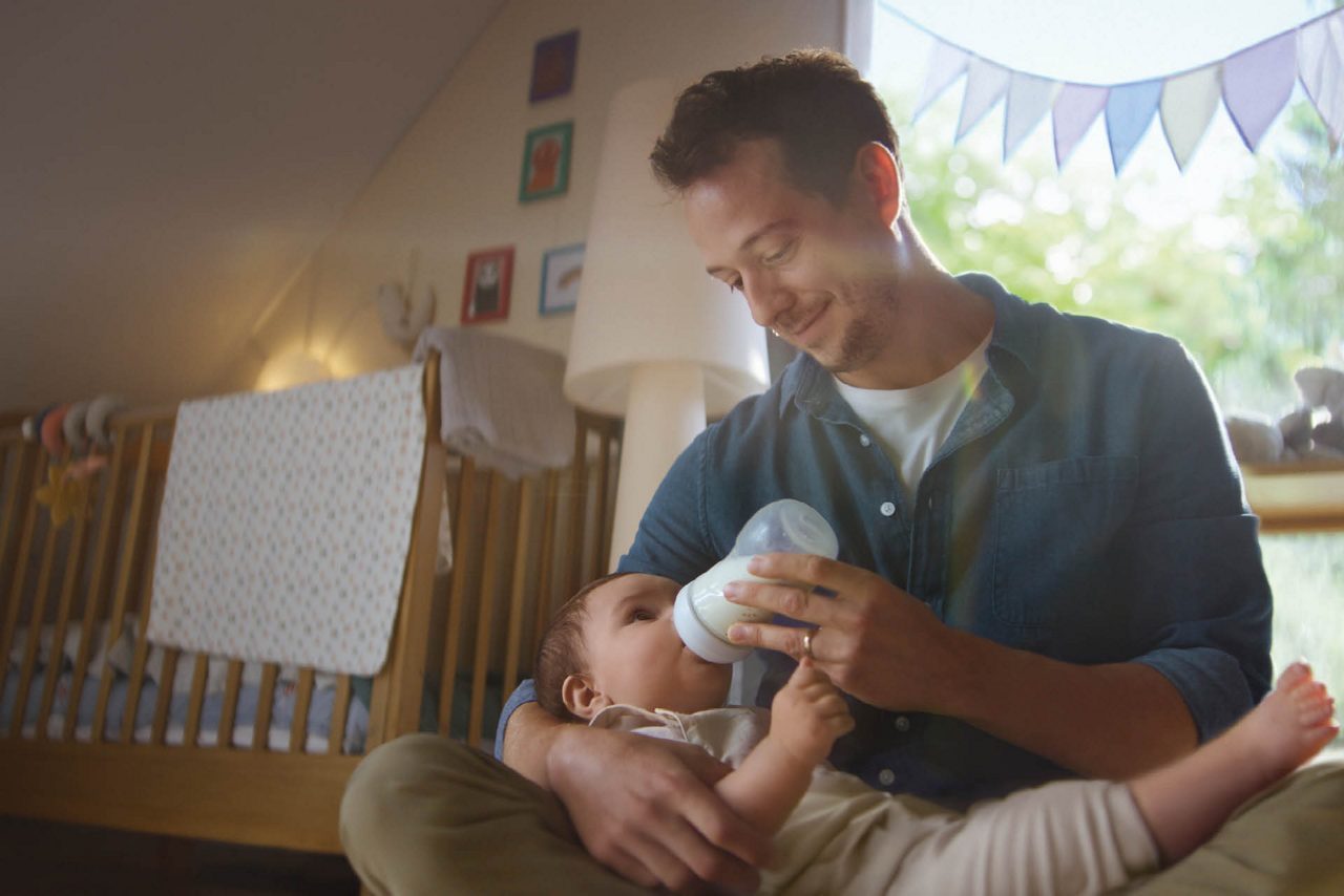 Vater füttert Baby mit Flasche im Kinderzimmer