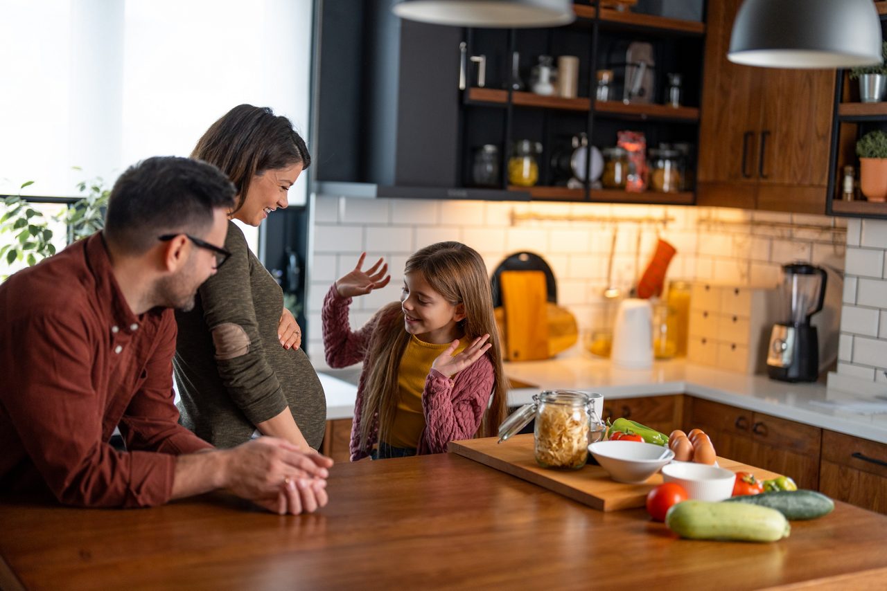 Eltern mit Tochter in der Küche spricht mit Baby im Bauch 