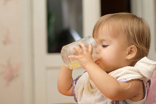 Toddler drinking a glass of orange juice