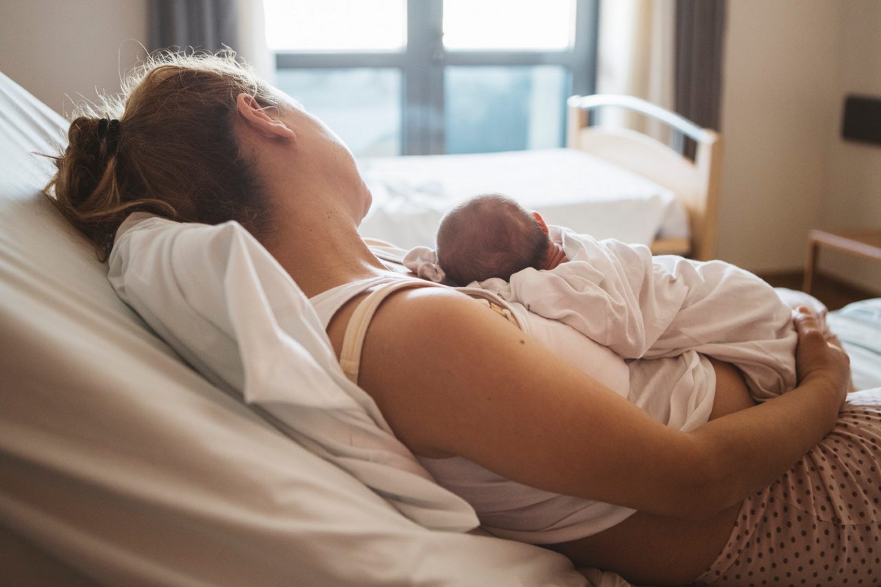 Mama mit Geburtsverletzungen liegt mit Baby im Krankenhausbett