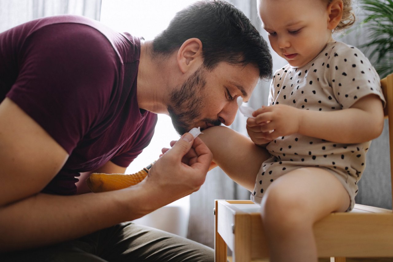 Vater küsst verletztes Kind mit Pflaster in der Hand