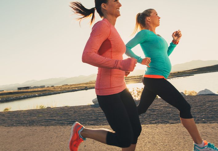 Two female runners in pink and blue athletic shirts are training for their next race. These women enjoy running at sunset in the evening together as friends on the trails through. Running is their way of staying active and healthy.