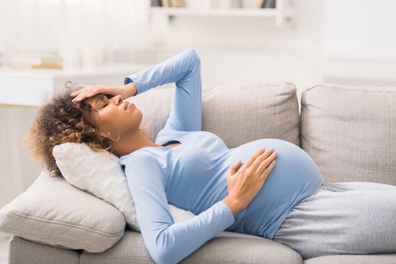 Schwangere liegt mit Kopfschmerzen auf Sofa