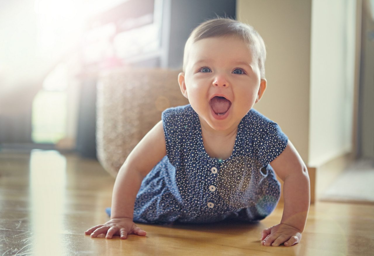Laughing baby crawling on the floor with blue dress