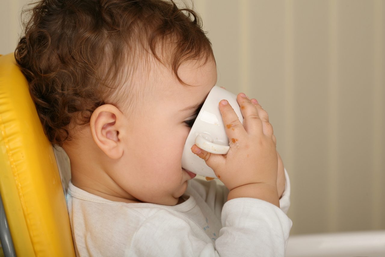 One year old toddler drinks milk from cup.