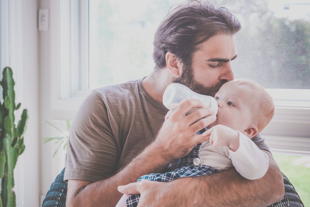 Vater füttert Baby ein Fläschen und küsst es auf den Kopf