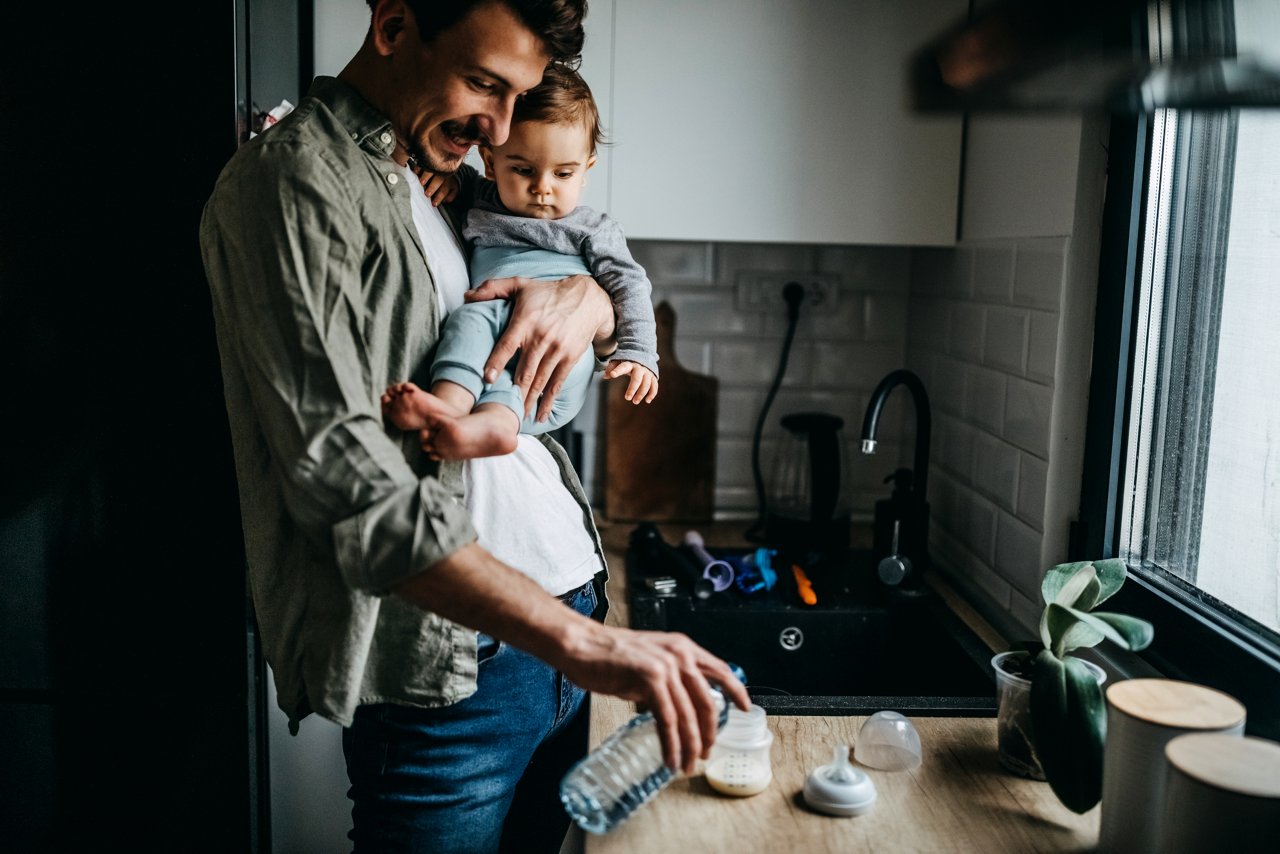 Father preparing the baby bottle for his baby in the kitchen