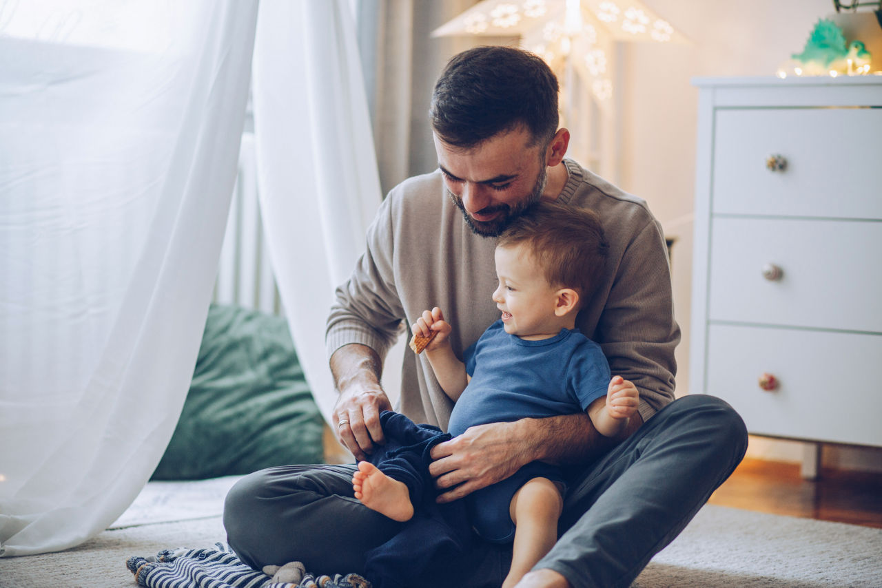 Father changing clothing to baby son, they are on floor and have good time