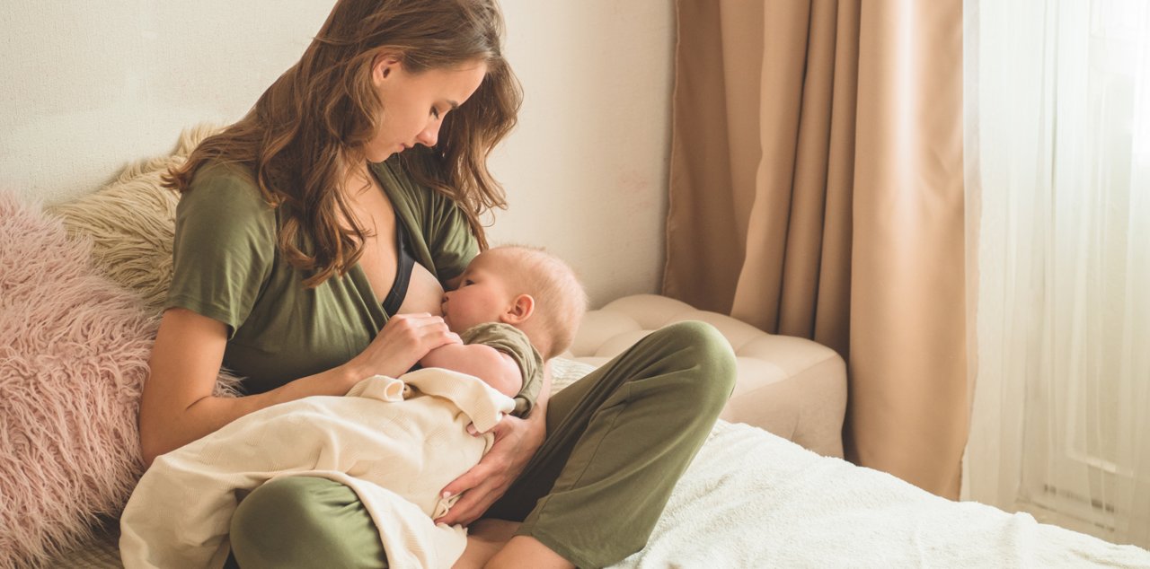 Mother sitting on bed breastfeeding her baby