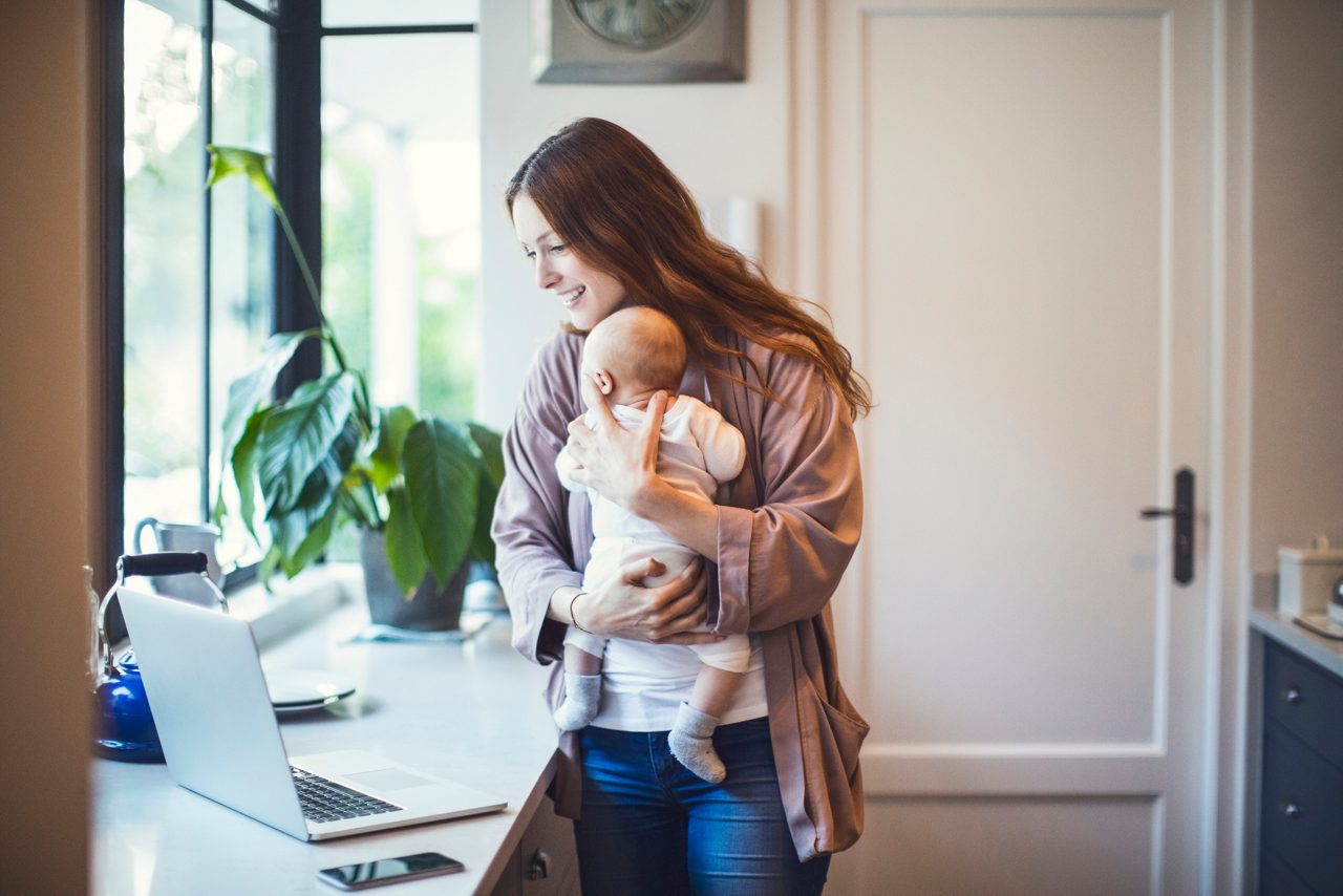 Mutter mit Baby schaut auf Laptop
