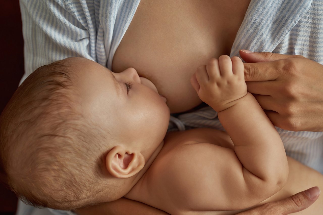 Portrait of sweet little child, breastfeeding and having nap in mother's arms. Cute naked baby holding tight mother's index finger. Closeup portrait.