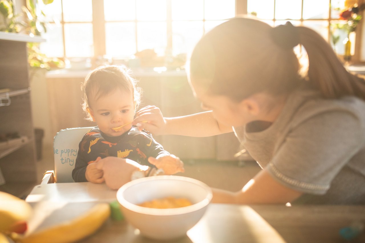 Mutter füttert Baby am Tisch.