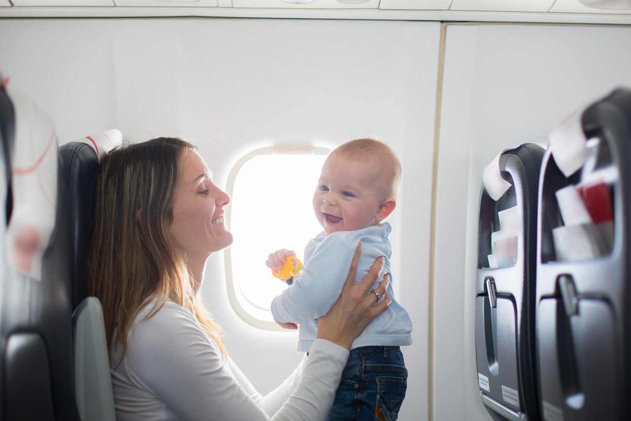 Young mom, playing and breastfeeding her toddler boy on board of aircraft, going on holiday