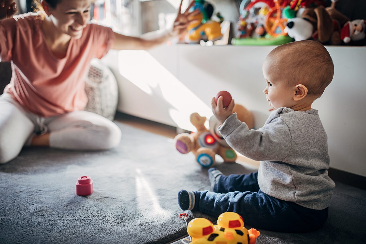 Two people, mother playing with her baby son on the floor in the living room at home.