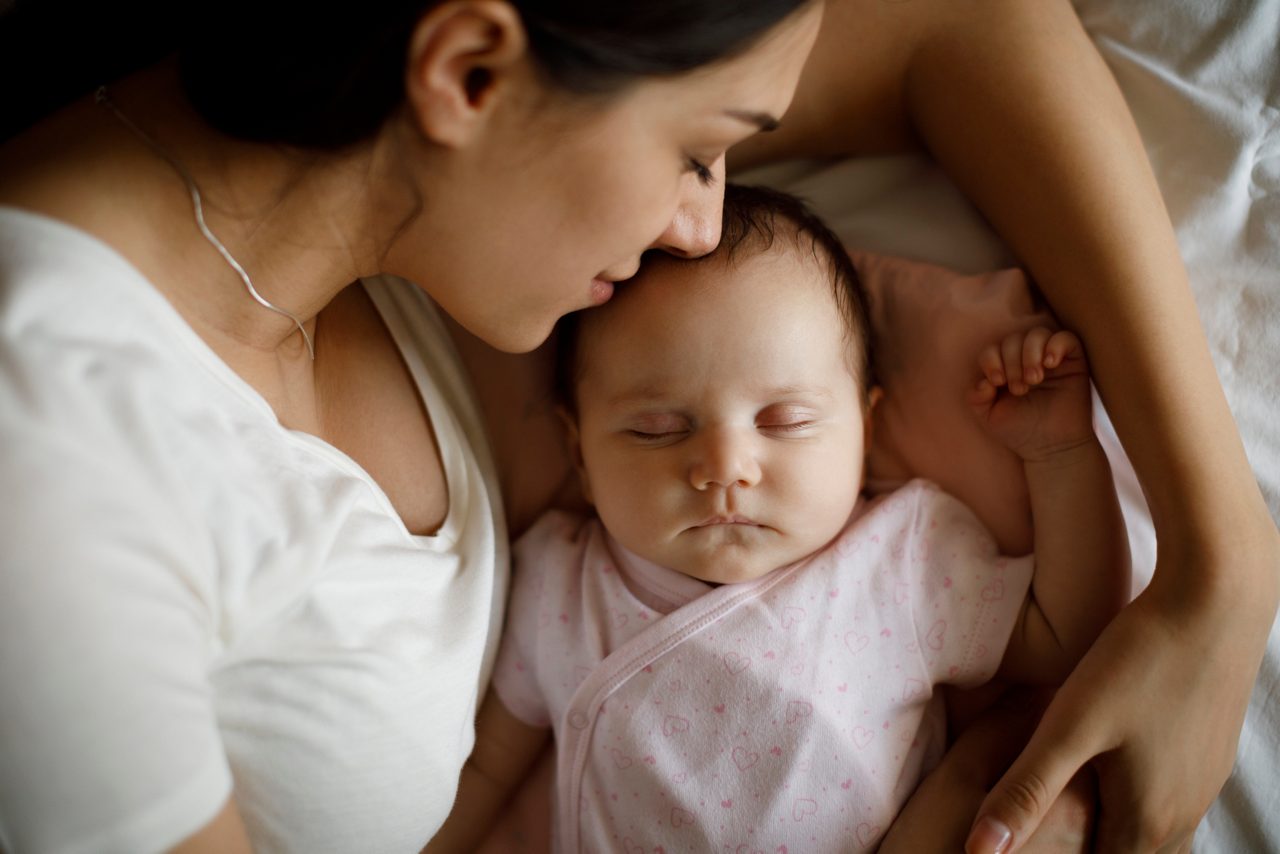 Beautiful young mother and her cute little baby sleeping in bed at home