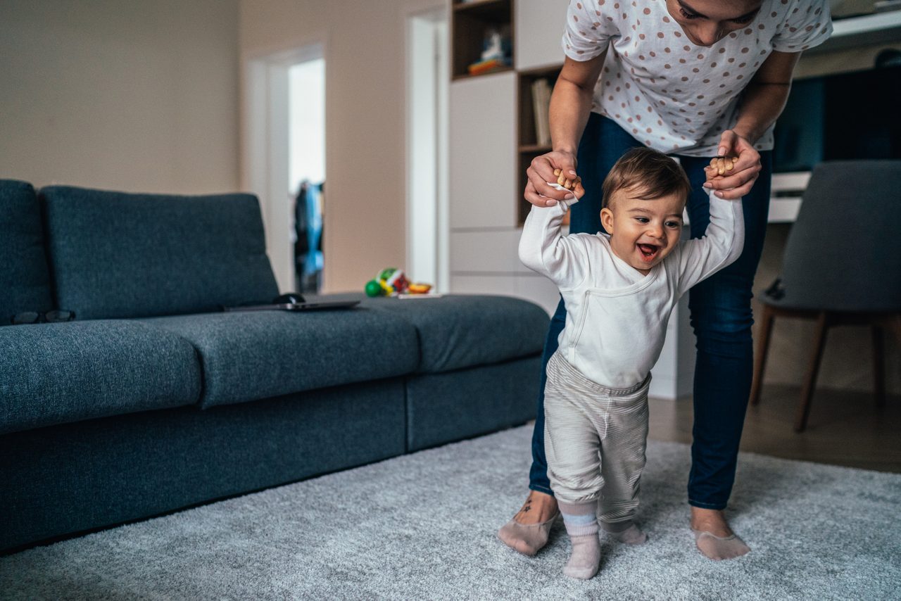 Mom teaches her baby son to walk and he enjoys the first steps