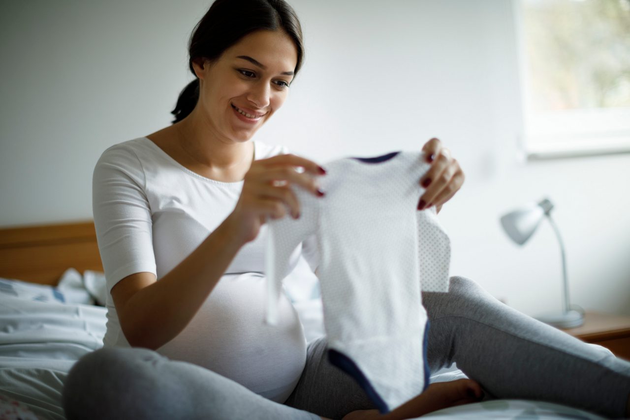 Schwangere hält einen Baby Strampler aus ihrer Erstausstattung