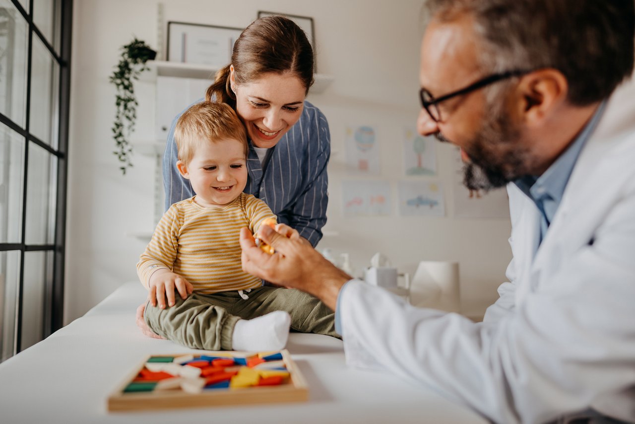 Doctor looking at playing toddler with mother